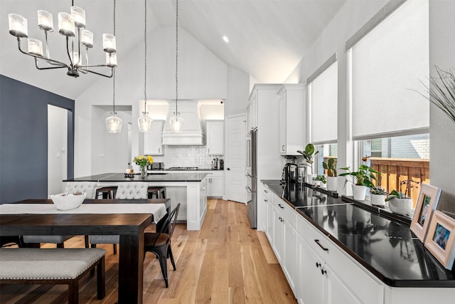 kitchen with white cabinets, dark countertops, a notable chandelier, high vaulted ceiling, and custom range hood