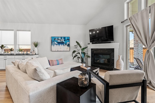 living room with a high end fireplace, high vaulted ceiling, and light wood finished floors