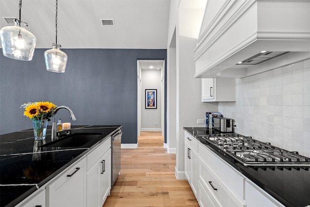kitchen with backsplash, appliances with stainless steel finishes, light wood-type flooring, a sink, and premium range hood