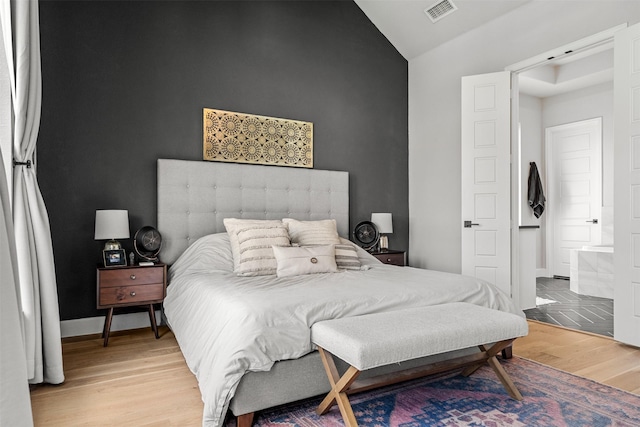 bedroom featuring baseboards, vaulted ceiling, light wood finished floors, and visible vents