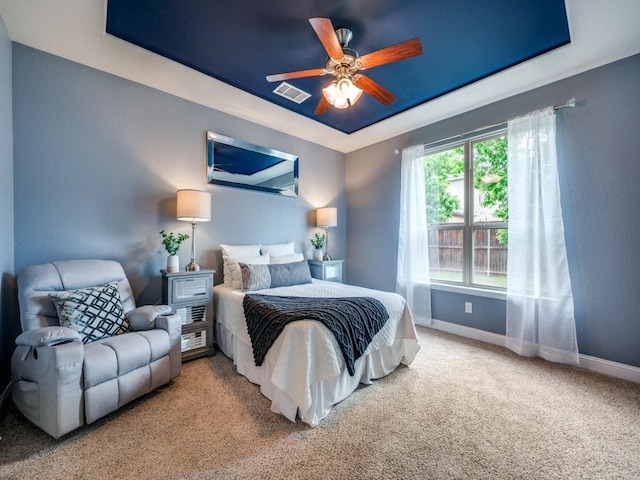 carpeted bedroom with a raised ceiling, baseboards, ceiling fan, and visible vents