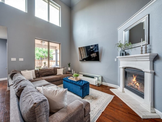 living room featuring a glass covered fireplace, baseboards, a high ceiling, and wood finished floors