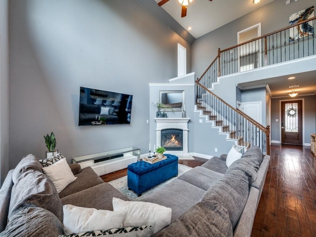 living room with a ceiling fan, baseboards, a glass covered fireplace, a high ceiling, and stairs