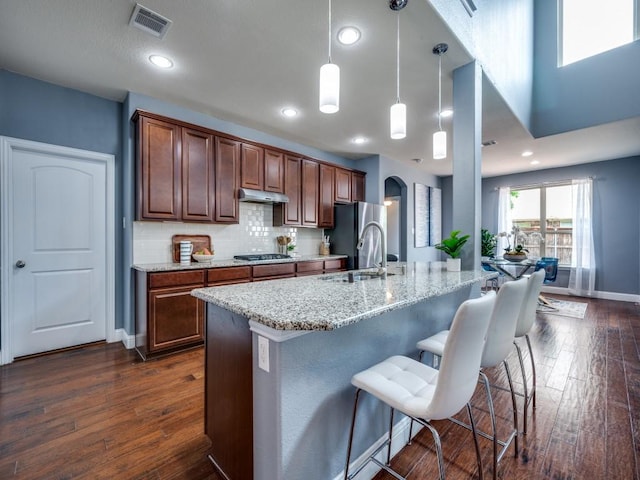 kitchen with visible vents, dark wood-style floors, under cabinet range hood, light stone counters, and stainless steel appliances