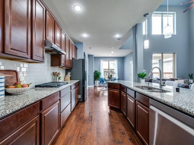 kitchen with a sink, light stone counters, dark wood-style floors, under cabinet range hood, and stainless steel appliances
