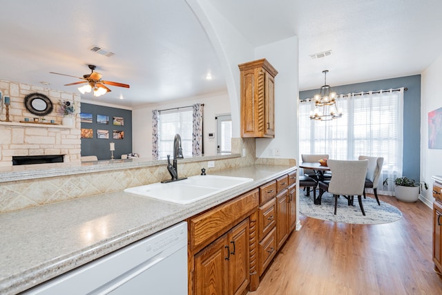 kitchen with visible vents, a stone fireplace, white dishwasher, a sink, and light wood-style flooring