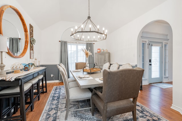 dining area featuring baseboards, a chandelier, arched walkways, light wood finished floors, and vaulted ceiling