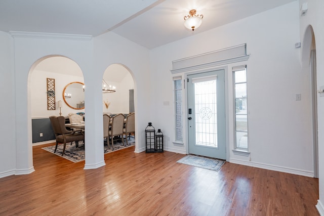 foyer entrance with light wood-style floors, arched walkways, baseboards, and a notable chandelier