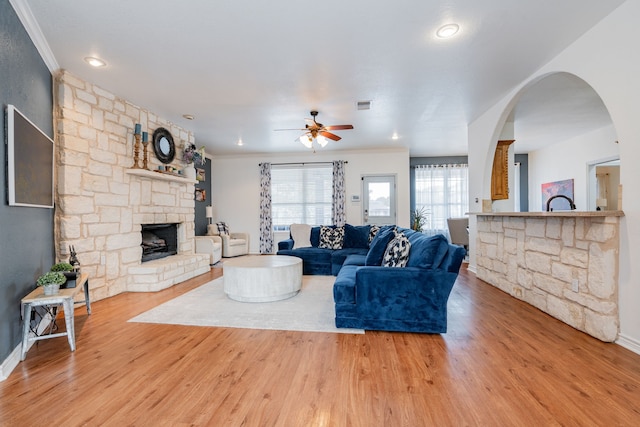living area with crown molding, ceiling fan, visible vents, and a stone fireplace