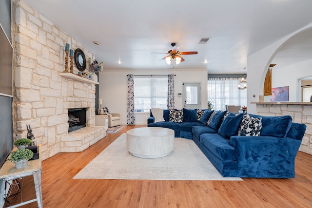 living area featuring visible vents, wood finished floors, a stone fireplace, arched walkways, and a ceiling fan