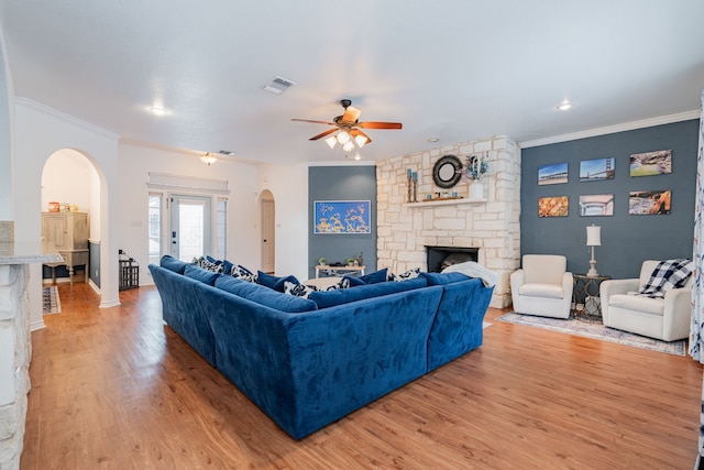 living area featuring a ceiling fan, ornamental molding, a fireplace, light wood-type flooring, and arched walkways