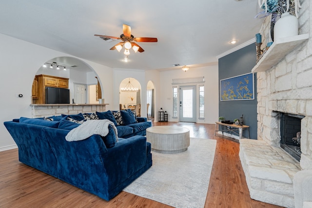 living area featuring wood finished floors, a fireplace, baseboards, ceiling fan, and arched walkways