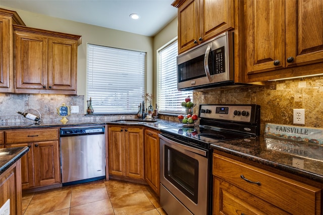 kitchen featuring appliances with stainless steel finishes, tasteful backsplash, brown cabinets, light tile patterned floors, and a sink