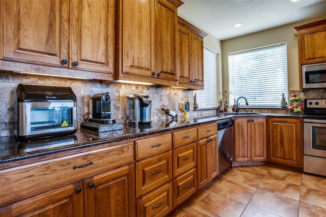 kitchen featuring decorative backsplash, brown cabinetry, a sink, light tile patterned floors, and stainless steel appliances