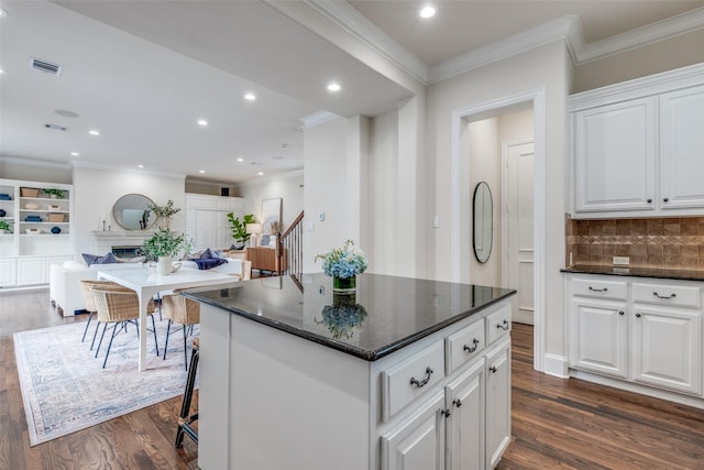 kitchen featuring visible vents, decorative backsplash, crown molding, a center island, and dark wood finished floors