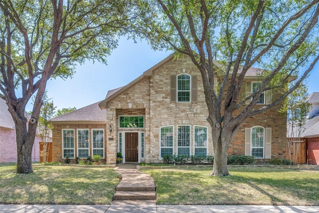 traditional home with brick siding, fence, stone siding, and a front lawn