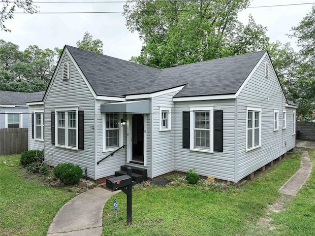 view of front of house featuring entry steps, fence, a shingled roof, and a front lawn