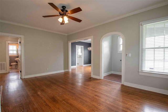 empty room with visible vents, ornamental molding, wood finished floors, ceiling fan, and arched walkways