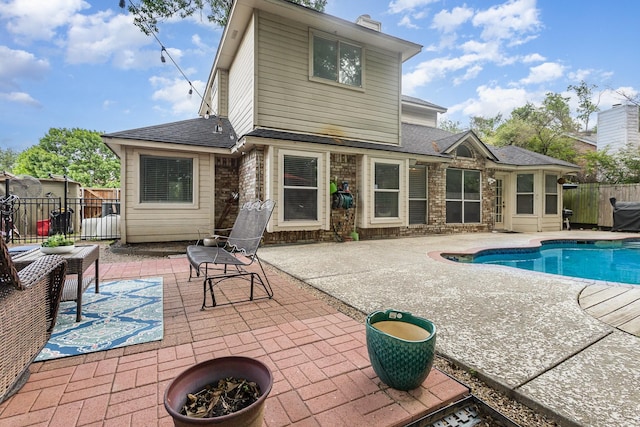 rear view of house featuring fence, a patio, brick siding, a shingled roof, and a fenced in pool