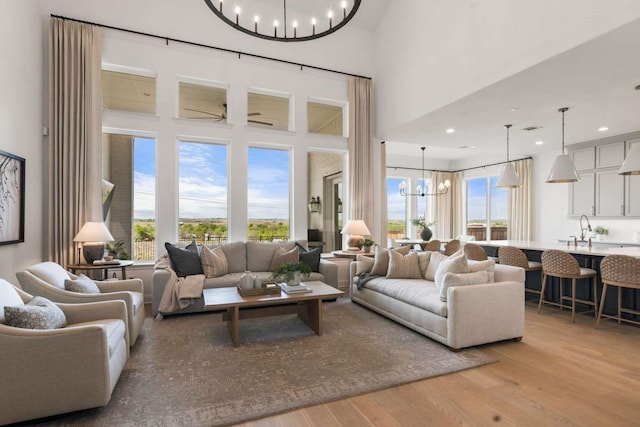 living area with visible vents, a high ceiling, a chandelier, and light wood finished floors