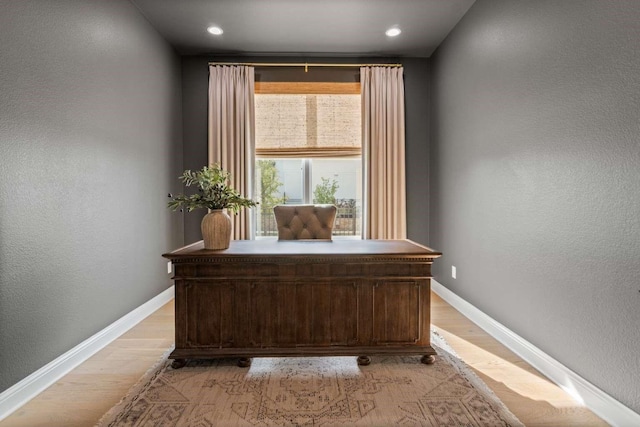 home office featuring baseboards, a textured wall, and light wood-style flooring