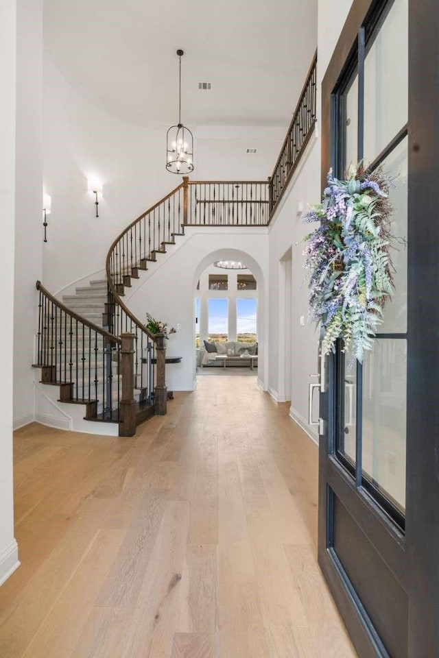 entrance foyer featuring a towering ceiling, arched walkways, wood finished floors, an inviting chandelier, and stairs