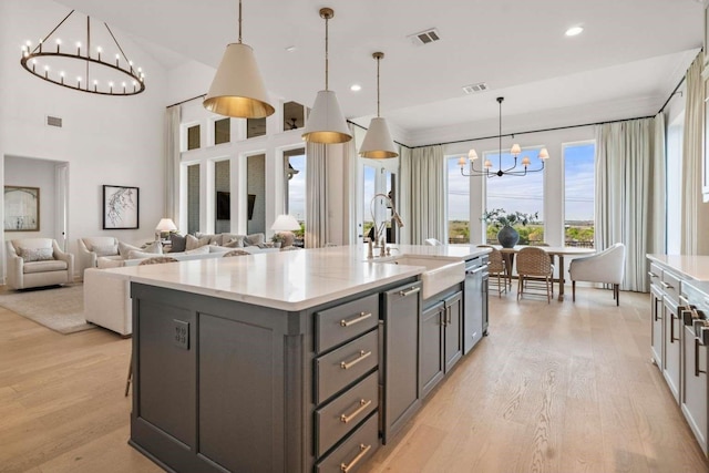kitchen with gray cabinetry, a kitchen island with sink, light wood finished floors, and a notable chandelier