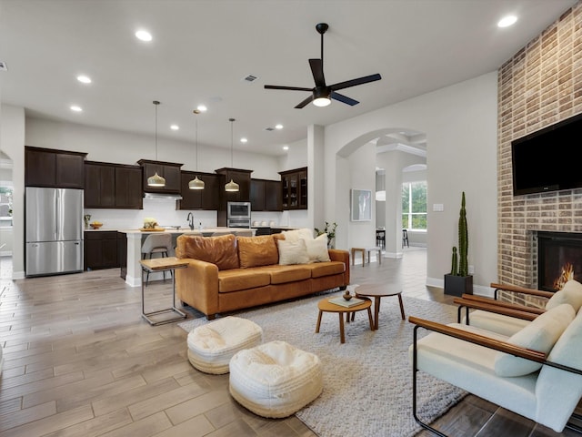 living area featuring visible vents, a fireplace, ceiling fan, light wood-type flooring, and arched walkways