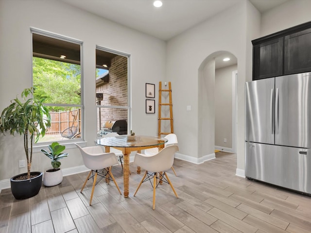 dining room with light wood-type flooring, arched walkways, baseboards, and a healthy amount of sunlight