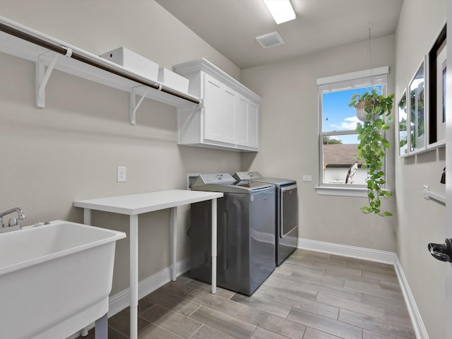 clothes washing area with cabinet space, a sink, baseboards, separate washer and dryer, and light wood-style flooring