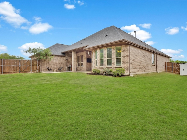back of house featuring a fenced backyard, a shingled roof, a lawn, and brick siding
