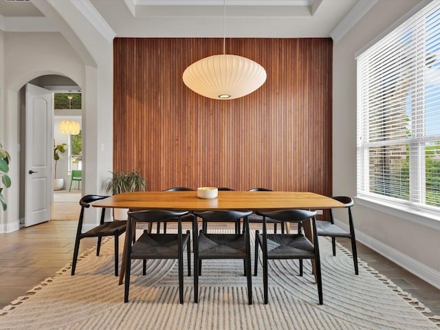 dining space featuring baseboards, arched walkways, a tray ceiling, and wood walls