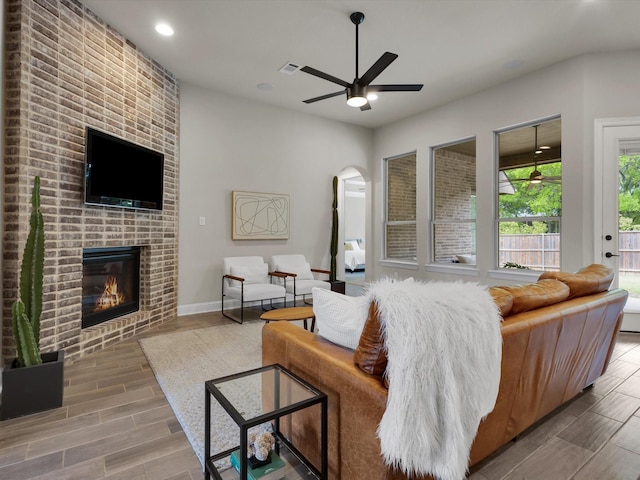 living room featuring arched walkways, a fireplace, a ceiling fan, and wood finish floors
