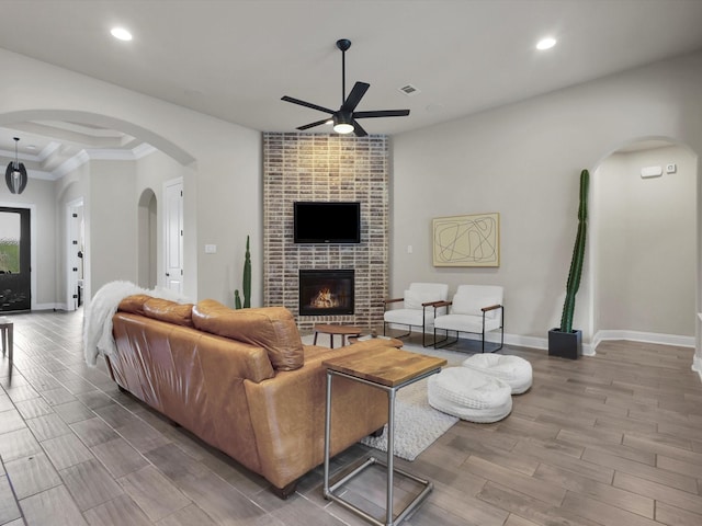 living room featuring a fireplace, arched walkways, a ceiling fan, baseboards, and wood finished floors