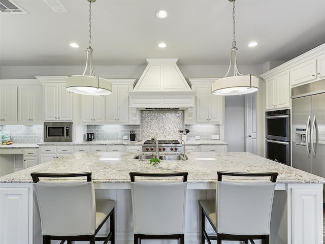 kitchen with visible vents, a sink, premium range hood, built in appliances, and an island with sink