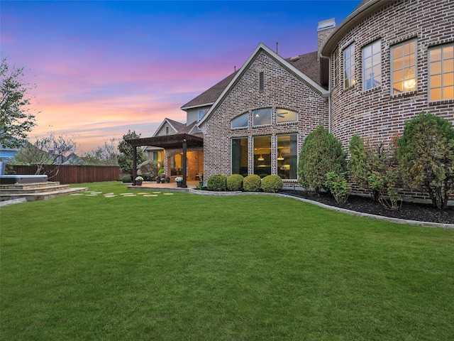 back of property featuring a lawn, brick siding, a chimney, and a patio