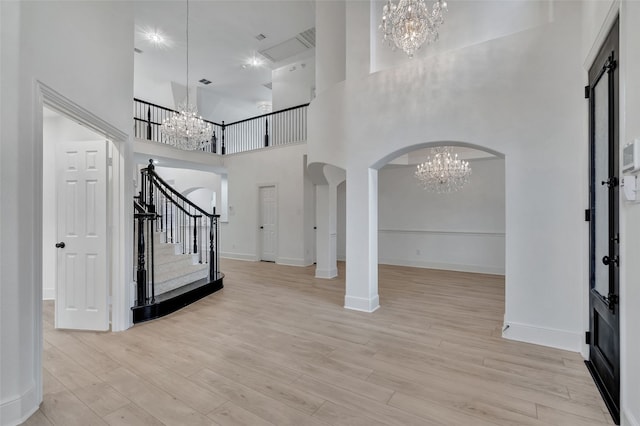 entrance foyer with arched walkways, stairway, light wood finished floors, an inviting chandelier, and a high ceiling