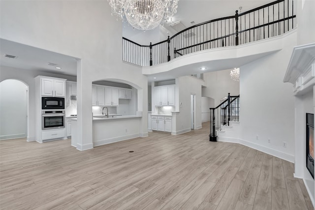 unfurnished living room featuring visible vents, a high ceiling, stairway, arched walkways, and a notable chandelier