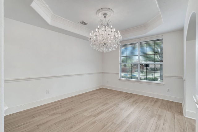 empty room with a raised ceiling, ornamental molding, and wood finished floors