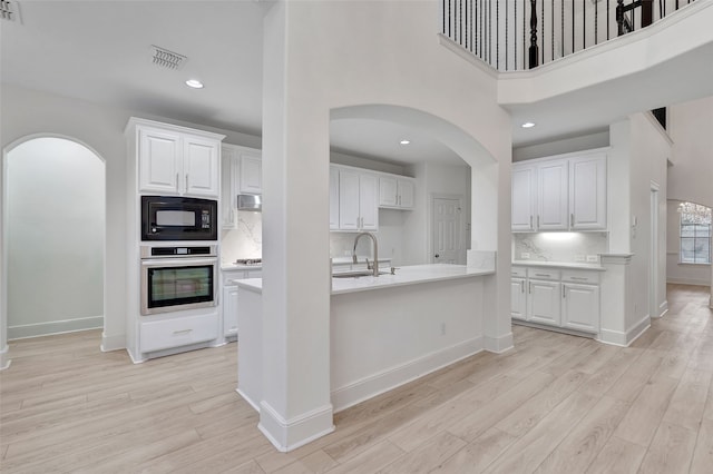 kitchen featuring a sink, light wood finished floors, light countertops, arched walkways, and stainless steel appliances