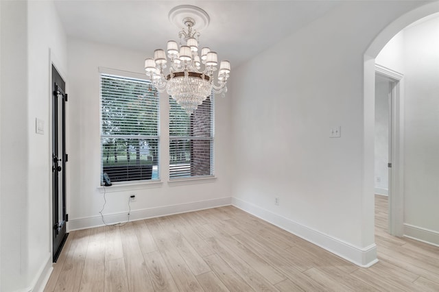unfurnished dining area with arched walkways, baseboards, light wood-style flooring, and a chandelier
