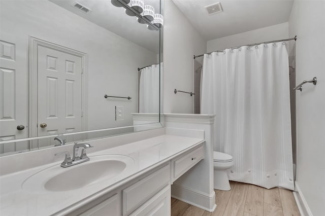 bathroom with vanity, toilet, wood finished floors, and visible vents