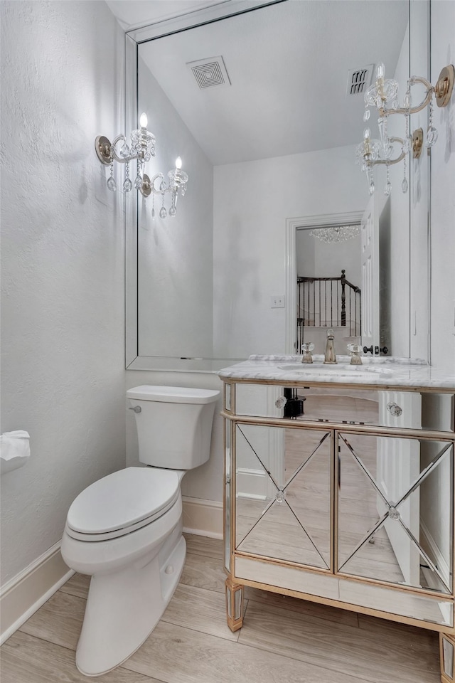 bathroom with baseboards, wood finished floors, visible vents, and toilet