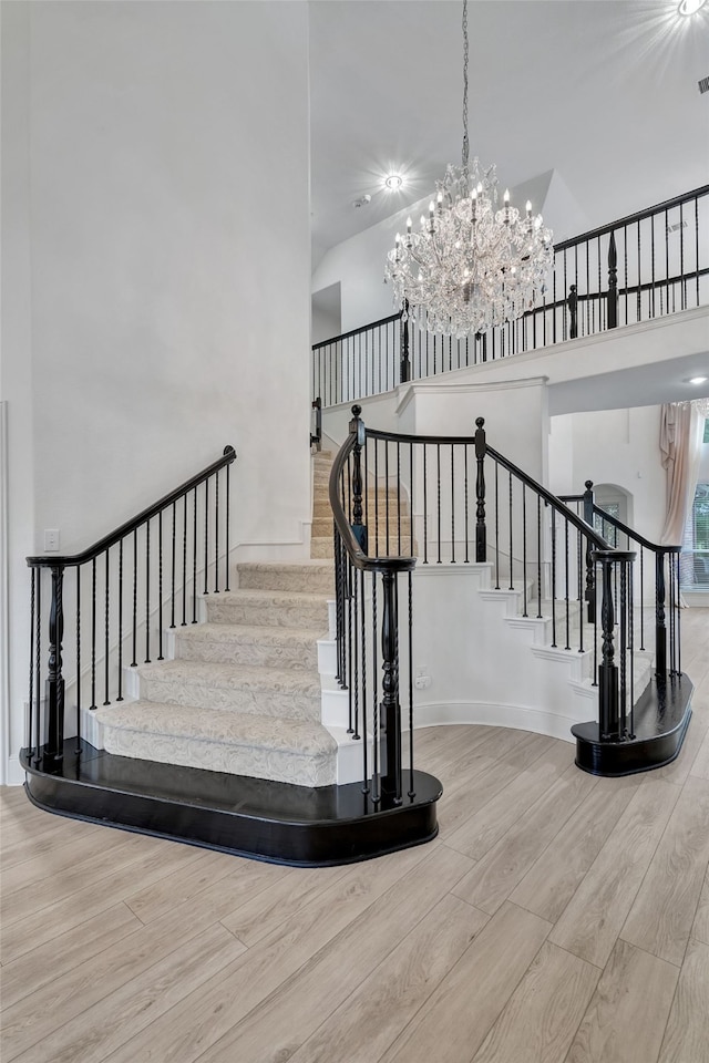 stairway featuring baseboards, a towering ceiling, wood finished floors, and a chandelier