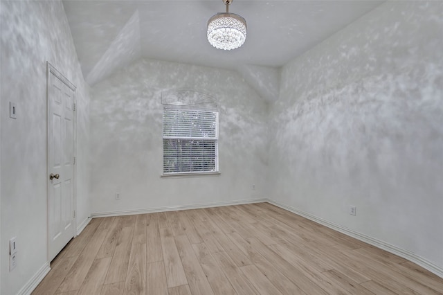spare room with baseboards, a notable chandelier, wood finished floors, and lofted ceiling