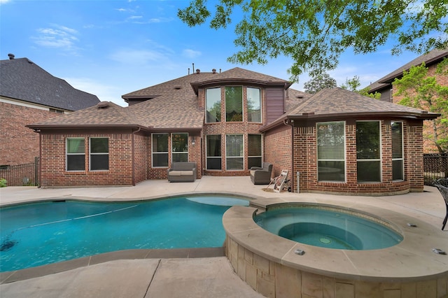 back of house with brick siding, roof with shingles, a patio area, and an in ground hot tub