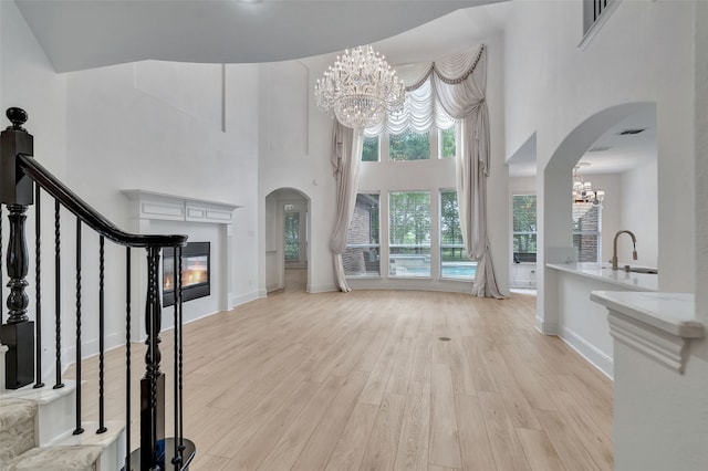 unfurnished living room with a high ceiling, arched walkways, a sink, light wood-style flooring, and a notable chandelier