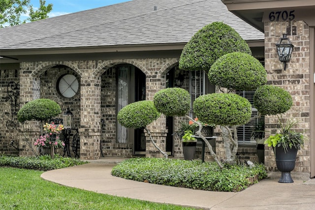 entrance to property with brick siding and a shingled roof