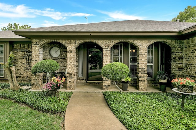 view of exterior entry featuring brick siding and a shingled roof