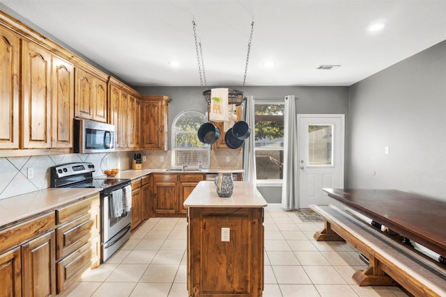 kitchen featuring brown cabinetry, a kitchen island, light countertops, backsplash, and stainless steel appliances